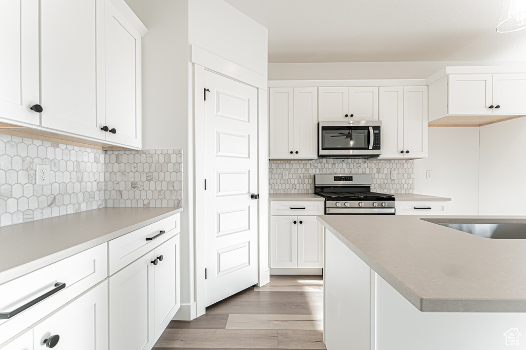 Kitchen featuring stainless steel appliances, light wood-type flooring, white cabinets, and light countertops