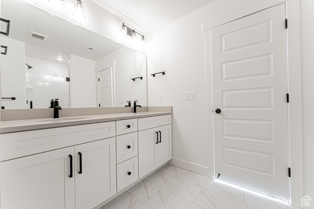Full bath with double vanity, a stall shower, marble look tile flooring, and baseboards
