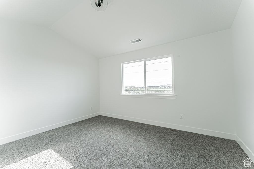 Empty room featuring lofted ceiling, baseboards, and dark carpet
