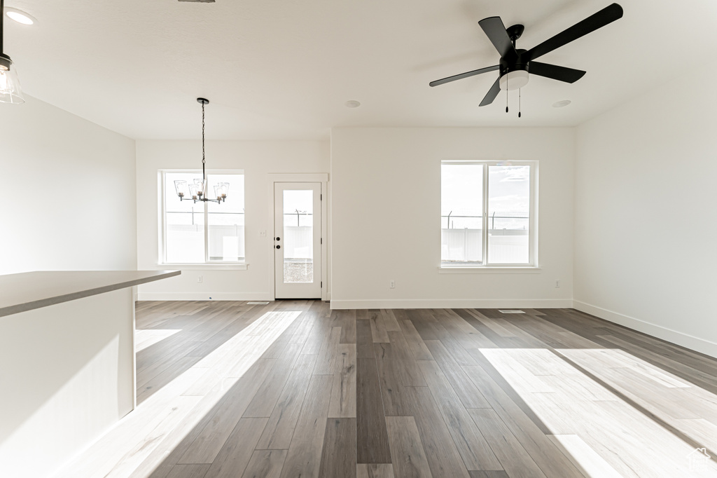 Unfurnished living room with a chandelier, healthy amount of natural light, baseboards, and wood finished floors