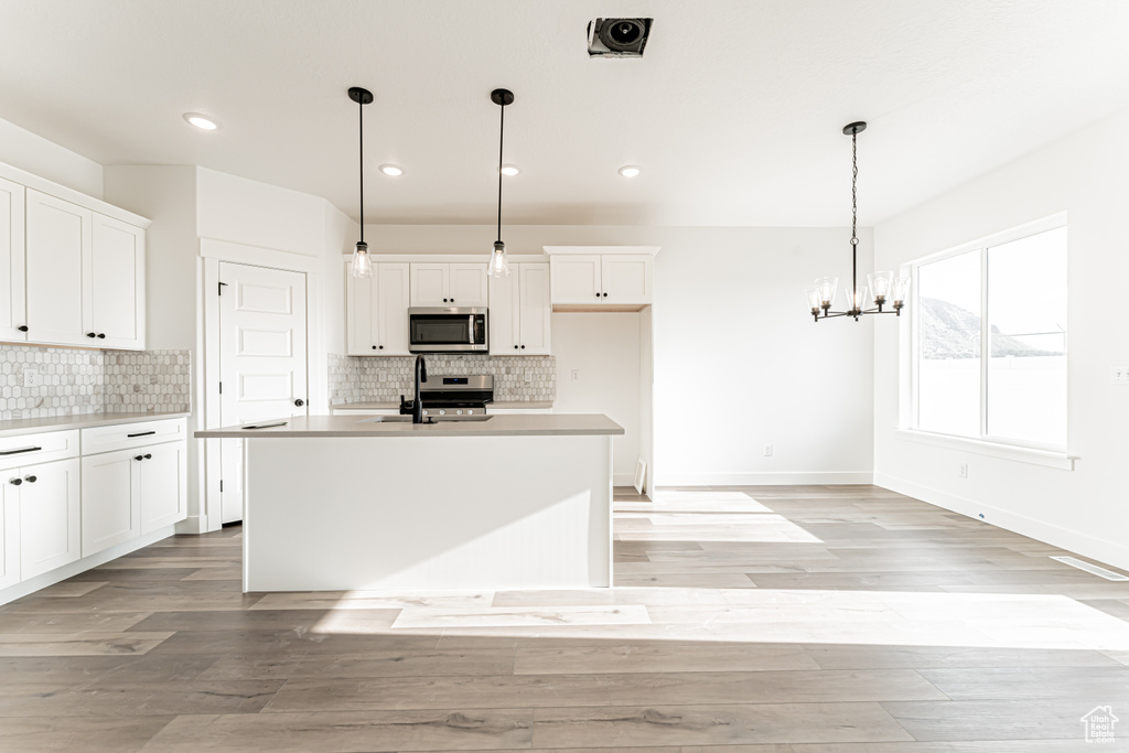 Kitchen with stainless steel appliances, white cabinets, backsplash, a chandelier, and recessed lighting