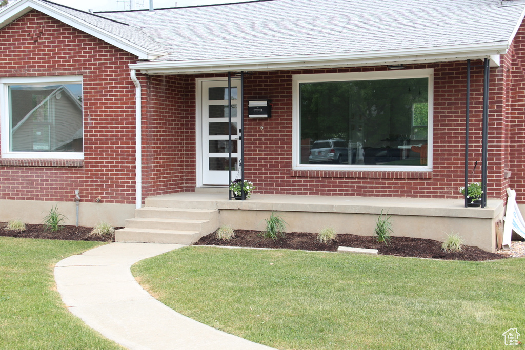 View of exterior entry with brick siding and roof with shingles
