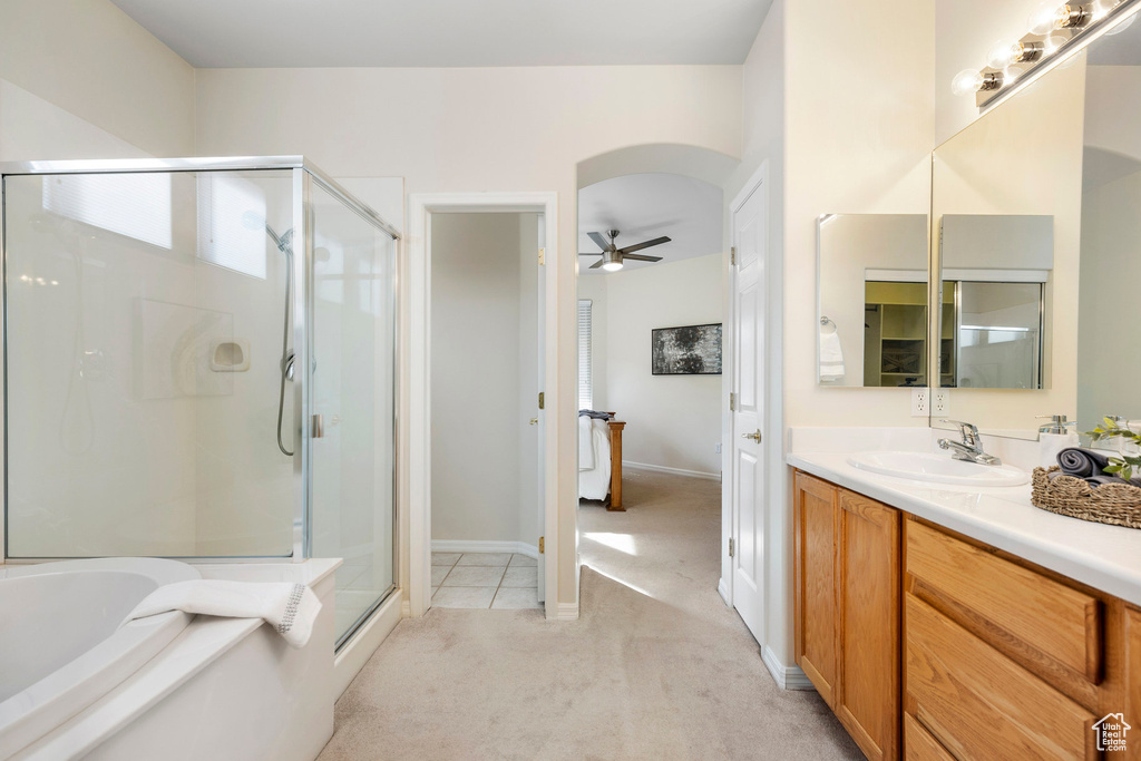 Full bath featuring a stall shower, a garden tub, ceiling fan, vanity, and baseboards