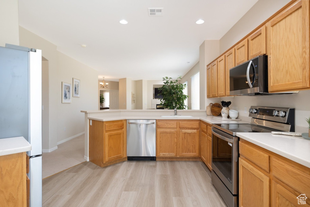 Kitchen with appliances with stainless steel finishes, light wood finished floors, a peninsula, a sink, and light countertops