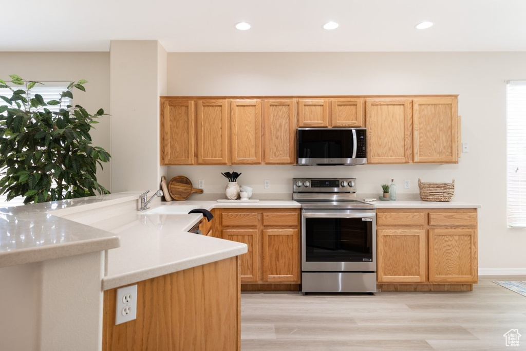 Kitchen with stainless steel appliances, a peninsula, light countertops, recessed lighting, and light wood finished floors