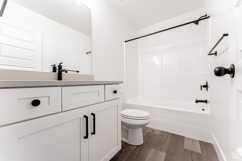 Bathroom with toilet, vanity,  shower combination, and wood finished floors