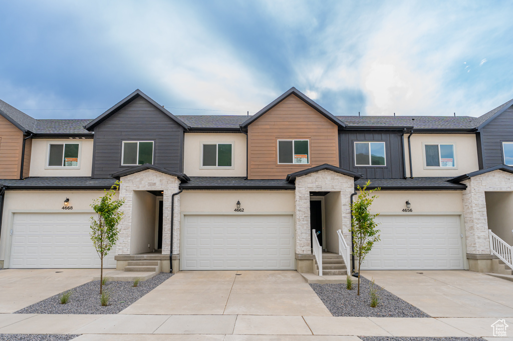 Townhome / multi-family property featuring an attached garage, stone siding, and concrete driveway