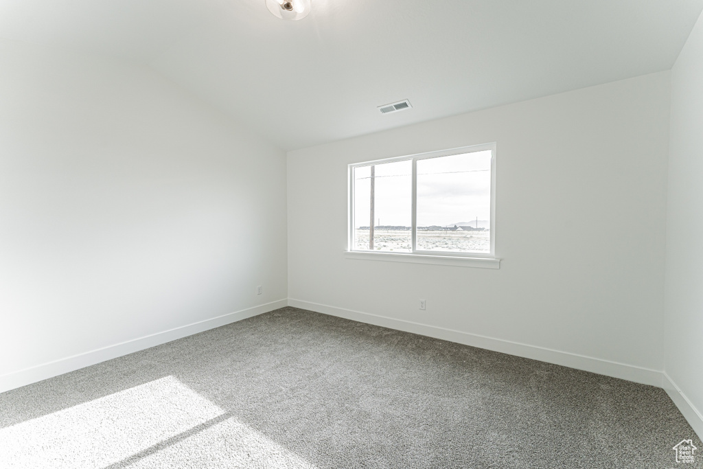 Spare room featuring dark carpet and lofted ceiling