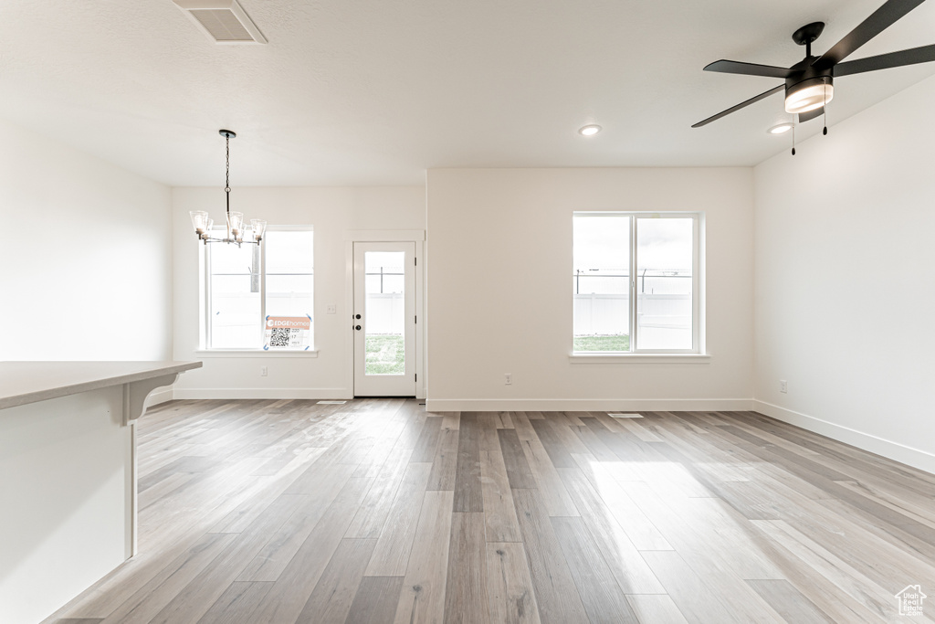 Unfurnished living room featuring a chandelier, light wood-type flooring, ceiling fan, and recessed lighting