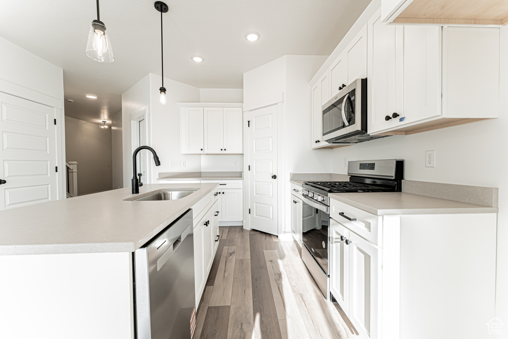 Kitchen with stainless steel appliances, a sink, light wood-style flooring, recessed lighting, and decorative light fixtures