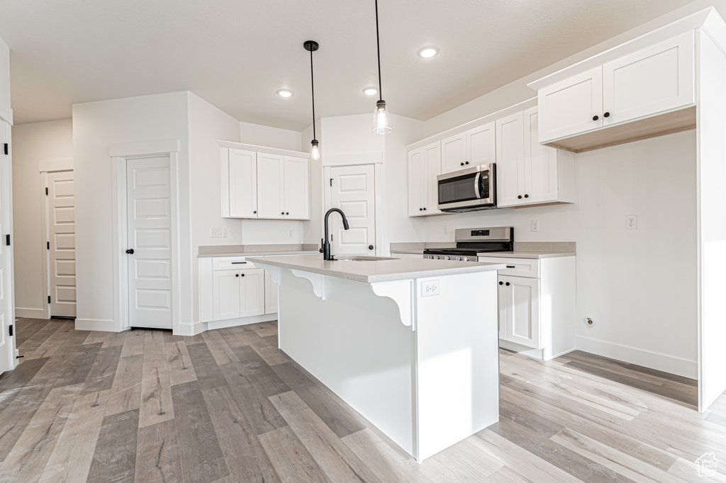 Kitchen with appliances with stainless steel finishes, recessed lighting, light wood finished floors, light countertops, and an island with sink
