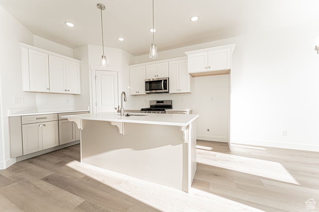 Kitchen featuring stainless steel appliances, a sink, light wood-style flooring, baseboards, and a kitchen island with sink