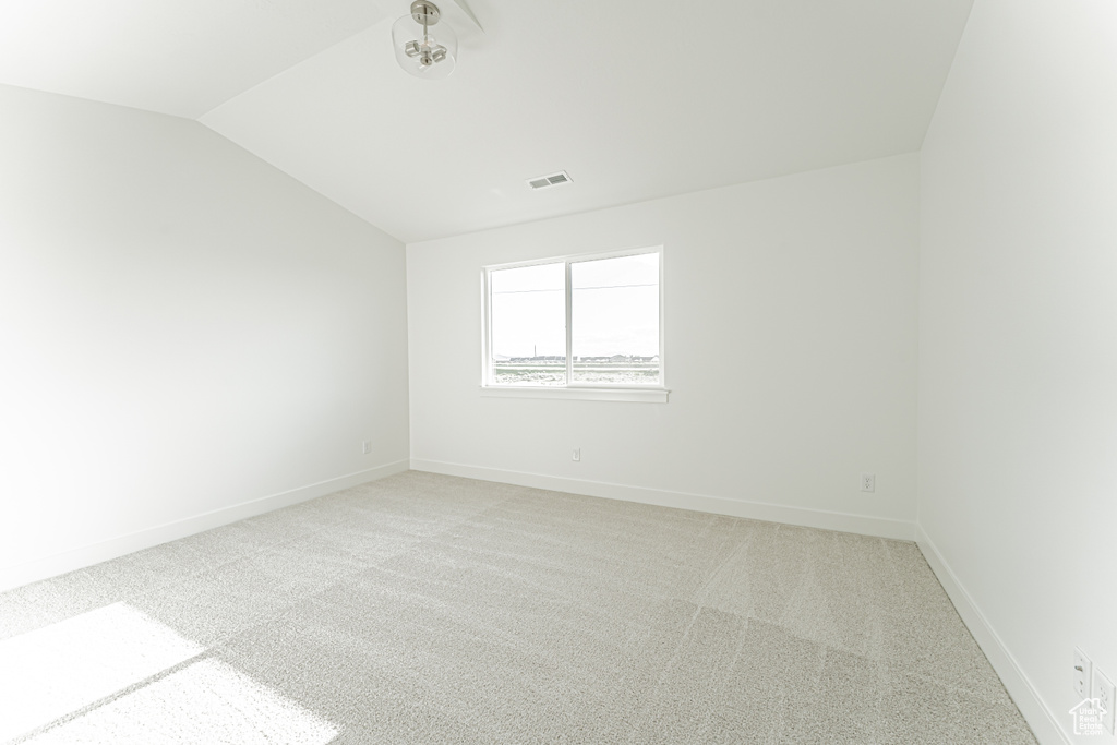 Spare room featuring light carpet, vaulted ceiling, and baseboards