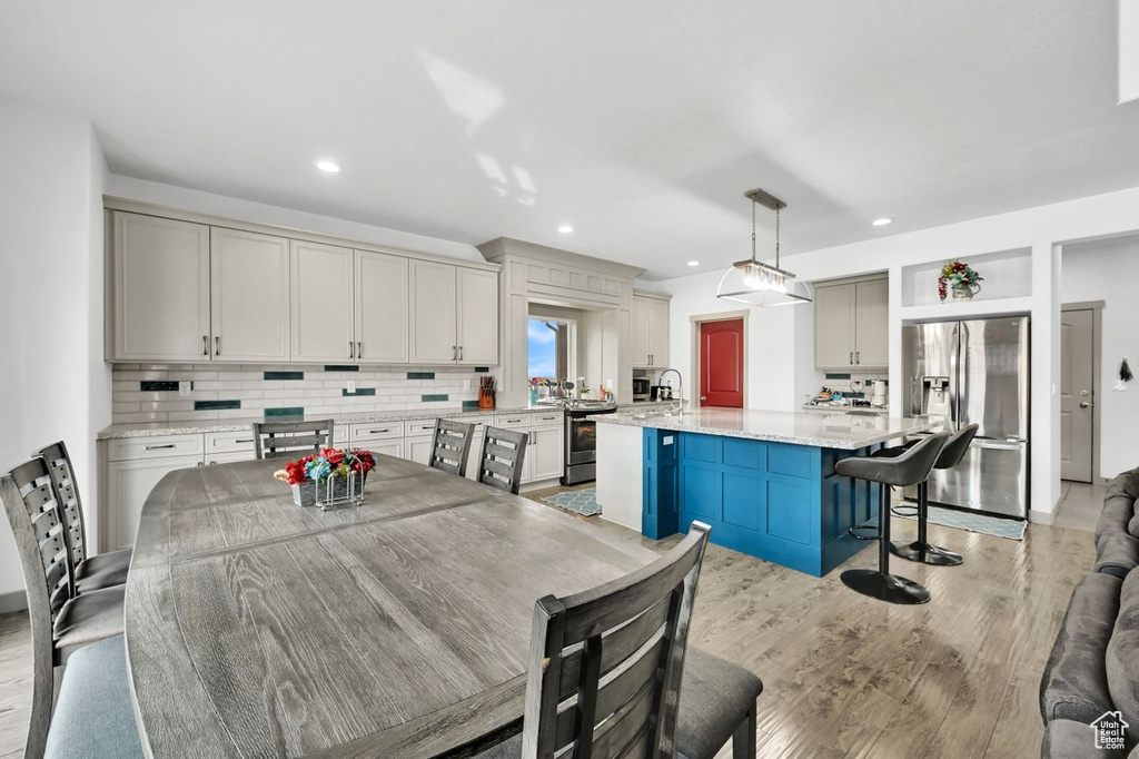 Kitchen with light stone counters, decorative light fixtures, a kitchen island, stainless steel appliances, and light hardwood / wood-style floors