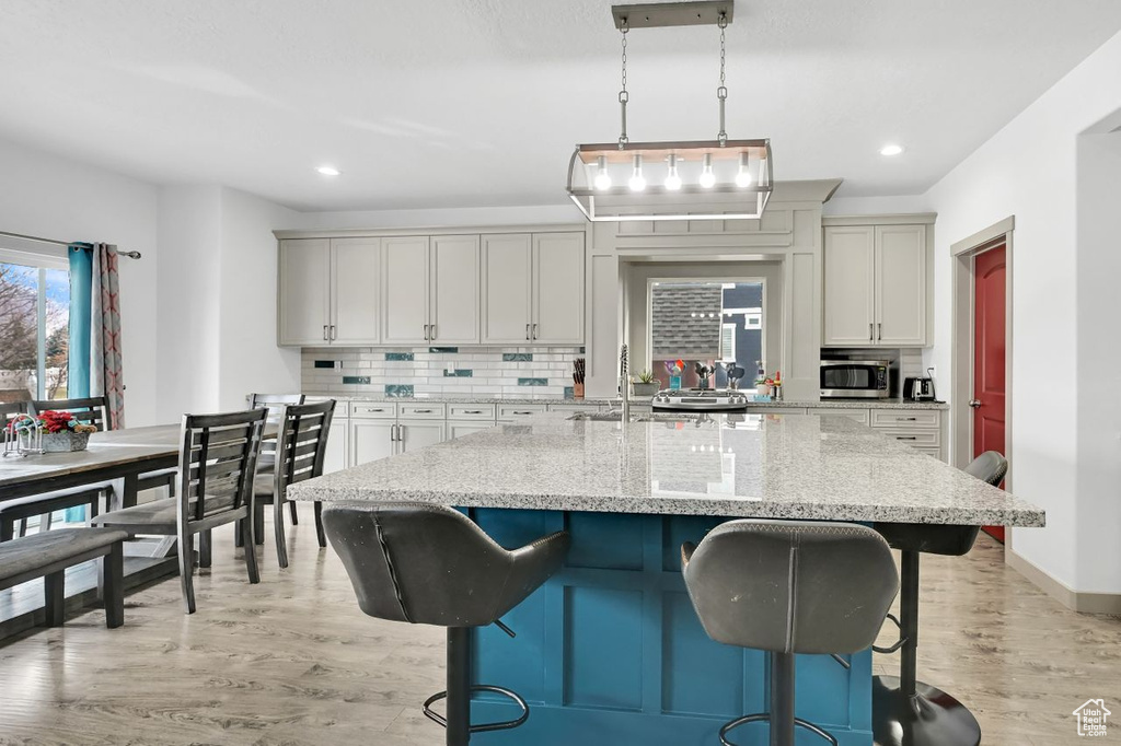 Kitchen with tasteful backsplash, decorative light fixtures, an island with sink, light stone countertops, and light hardwood / wood-style floors