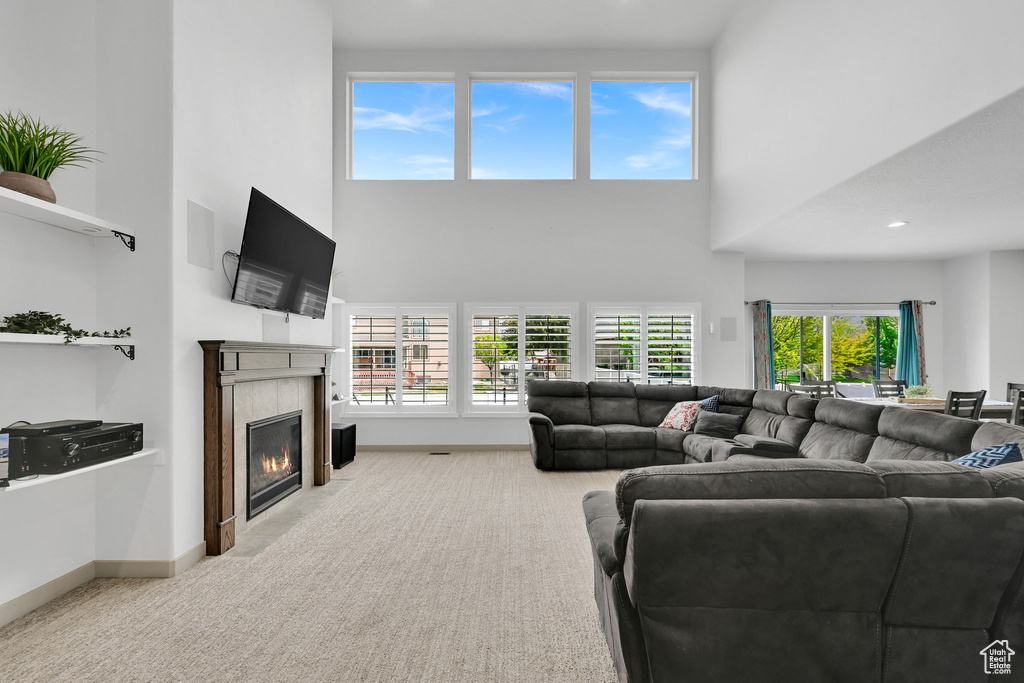 Carpeted living area featuring baseboards, a towering ceiling, and a tile fireplace