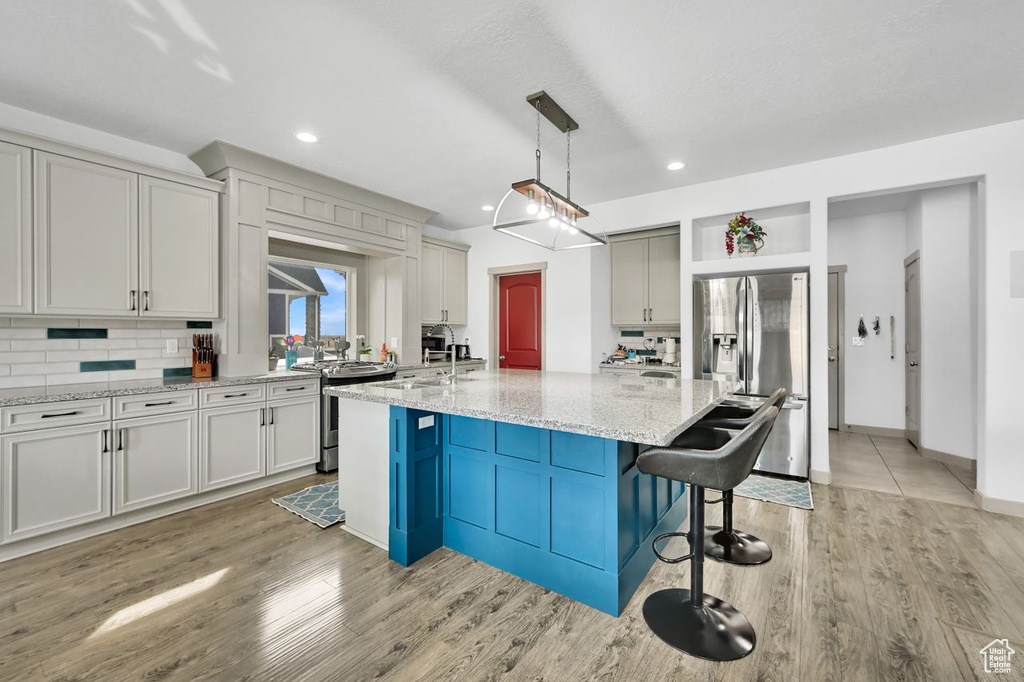 Kitchen with pendant lighting, a breakfast bar area, stainless steel appliances, tasteful backsplash, and a large island with sink