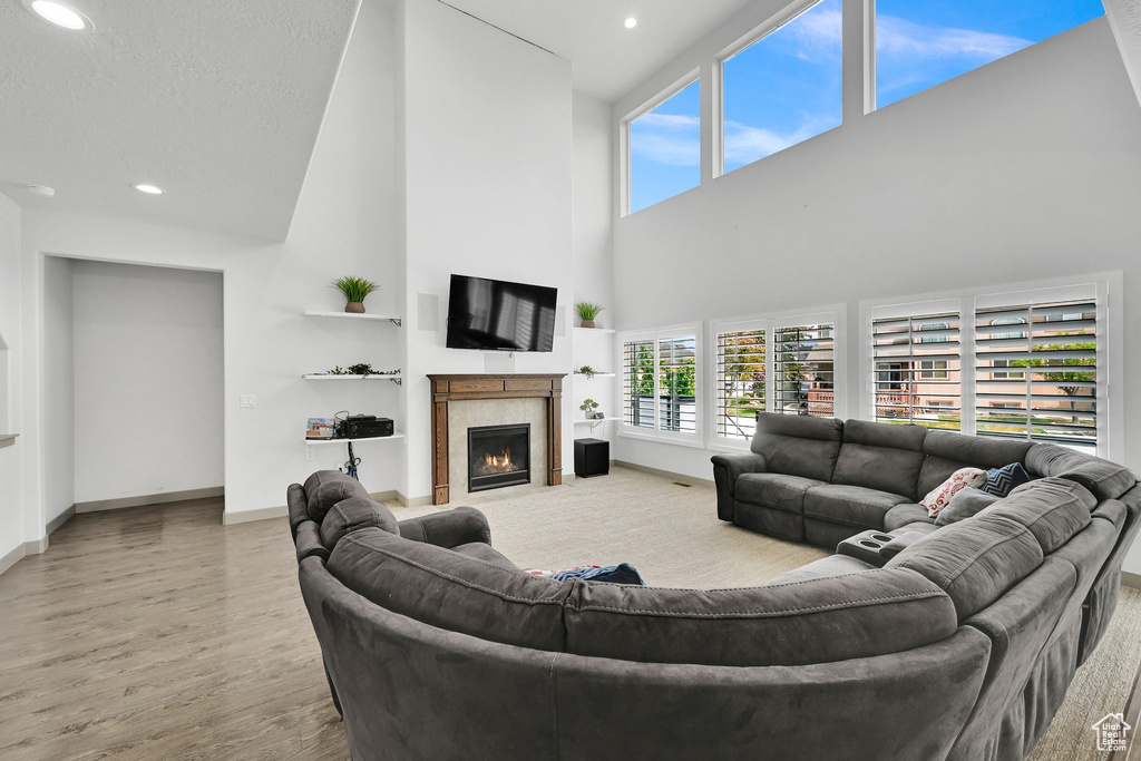 Living room with a tile fireplace, plenty of natural light, wood finished floors, and a towering ceiling