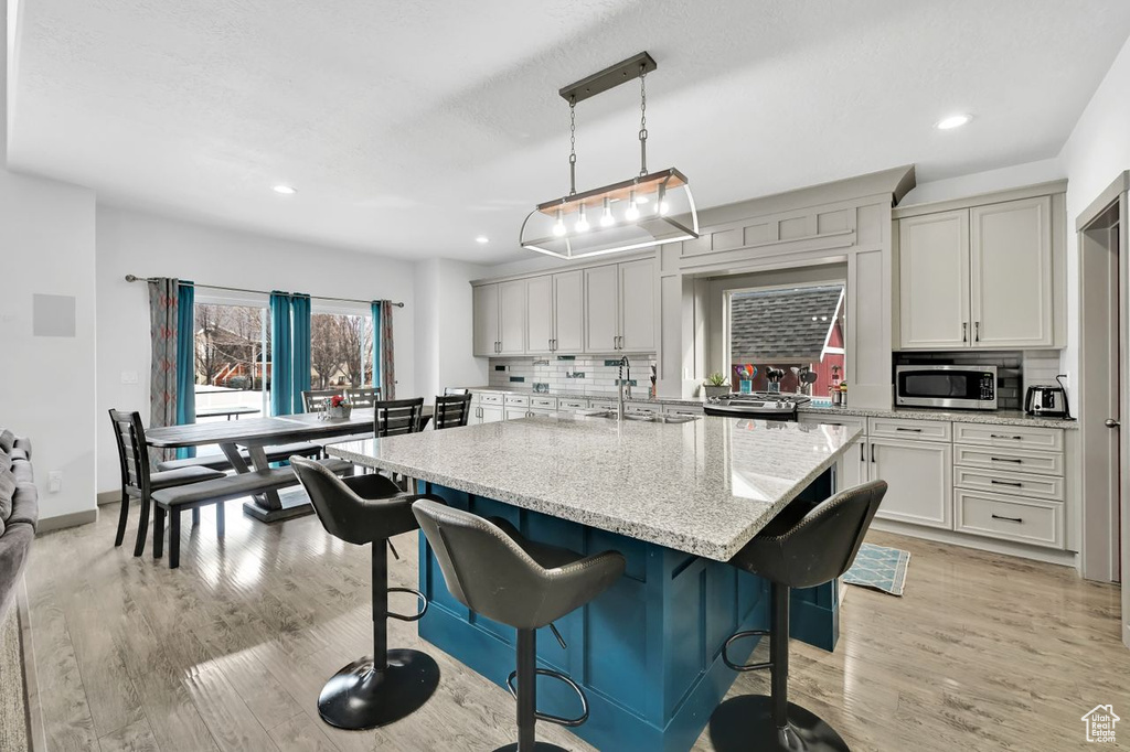 Kitchen featuring a kitchen island, decorative light fixtures, backsplash, light stone counters, and light wood-type flooring