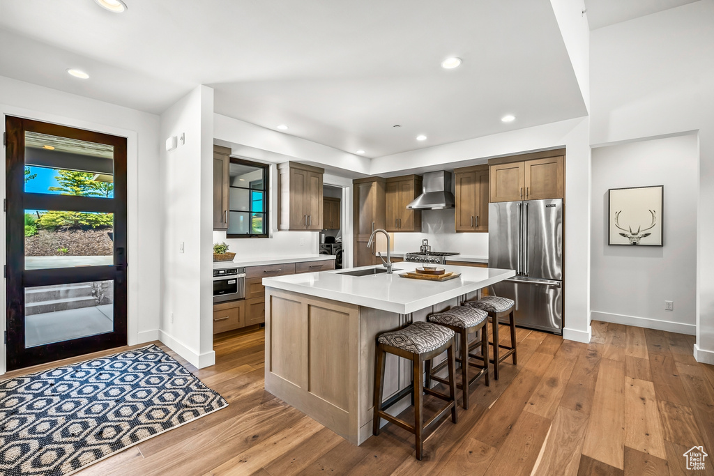 Kitchen with appliances with stainless steel finishes, light countertops, a sink, baseboards, and wall chimney exhaust hood