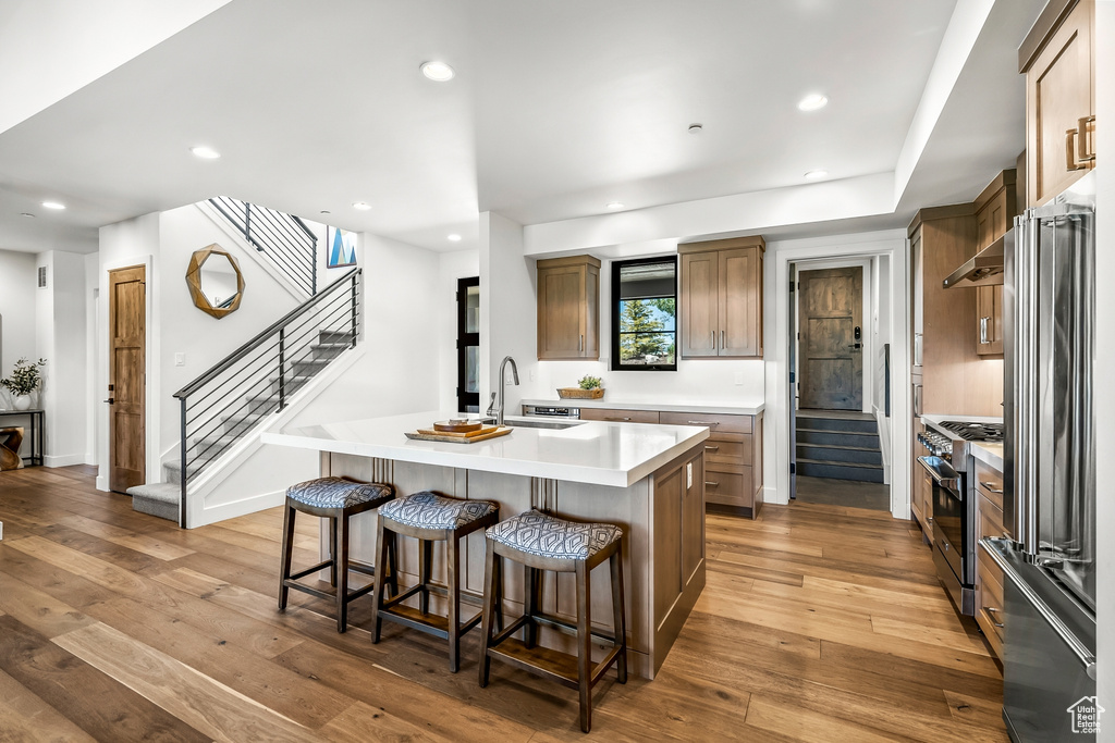 Kitchen with light wood-style flooring, high quality appliances, light countertops, a kitchen bar, and a center island with sink