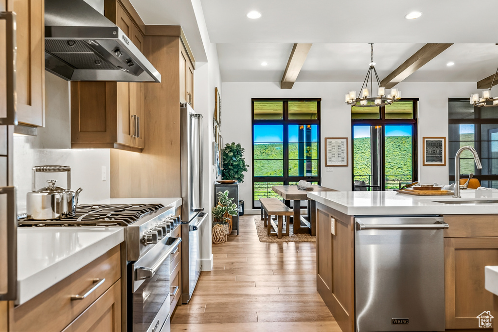 Kitchen featuring wall chimney range hood, beam ceiling, an inviting chandelier, and high end appliances