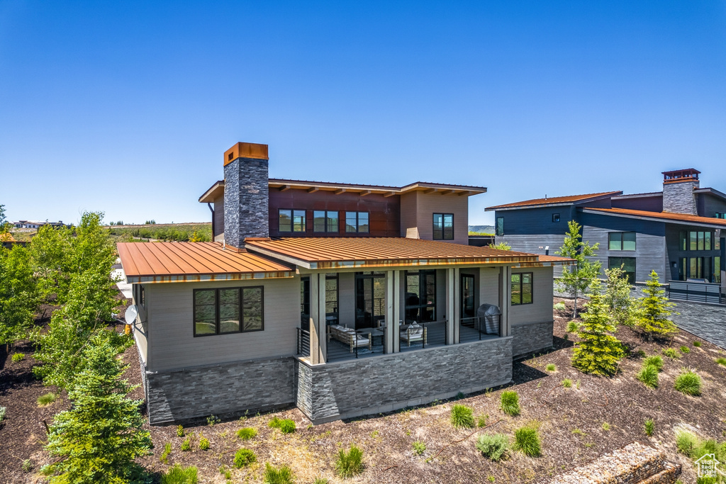 Rear view of house with metal roof, a standing seam roof, stone siding, and a chimney