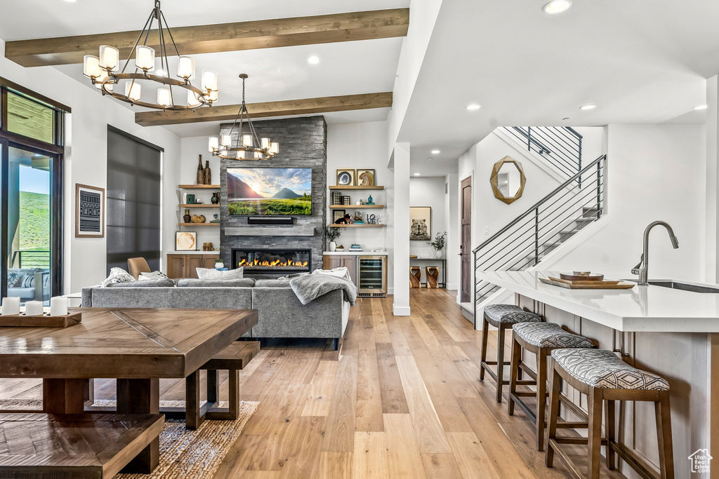 Living room with beamed ceiling, a notable chandelier, light wood-type flooring, stairs, and beverage cooler