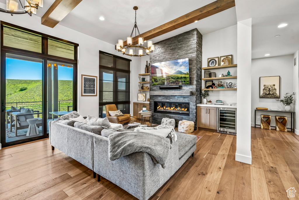 Living area featuring beamed ceiling, a chandelier, a fireplace, light wood-style floors, and beverage cooler