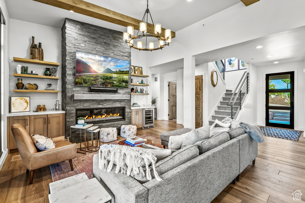 Living area featuring beverage cooler, wood finished floors, an inviting chandelier, a stone fireplace, and stairway