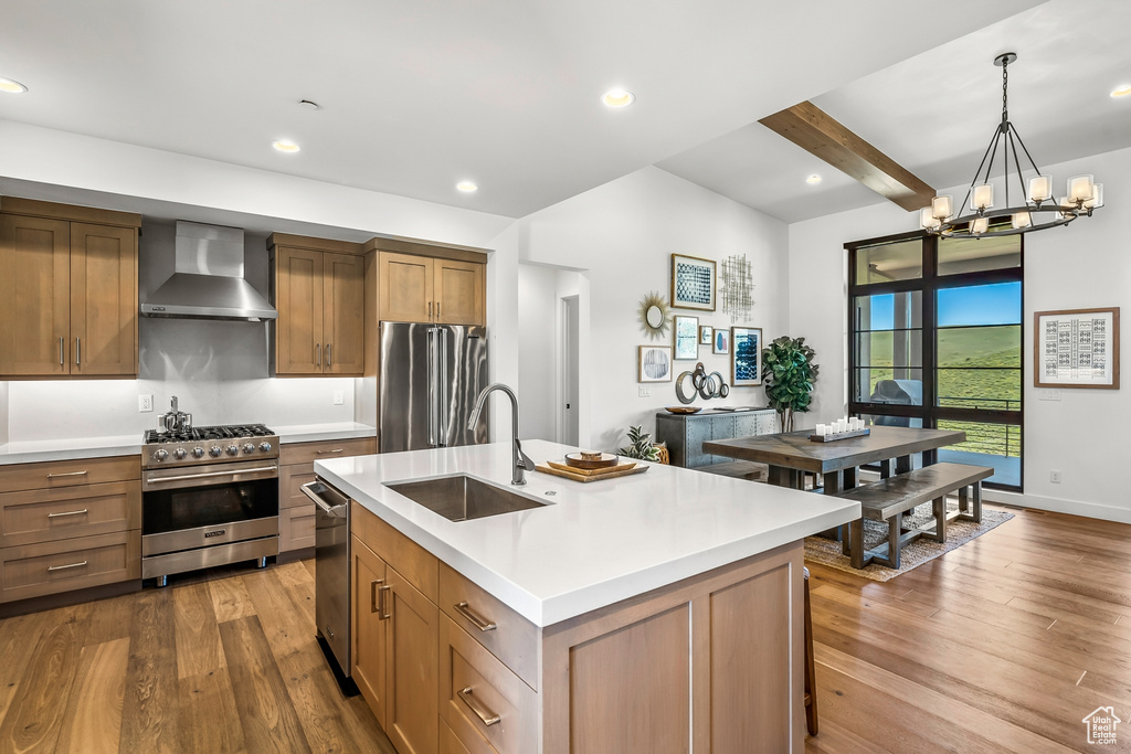 Kitchen featuring a sink, premium appliances, dark wood-style floors, an inviting chandelier, and wall chimney exhaust hood