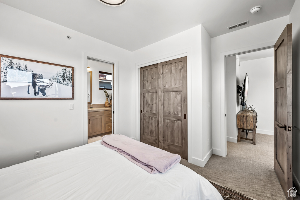Bedroom with a closet, visible vents, baseboards, carpet floors, and ensuite bathroom