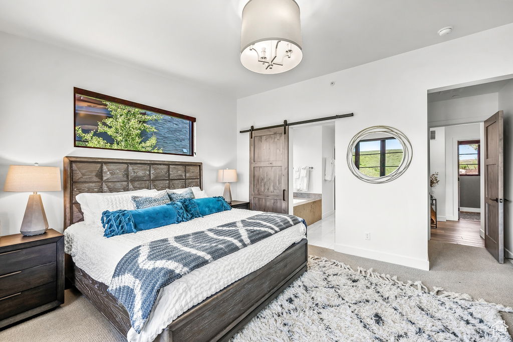 Bedroom featuring carpet, ensuite bath, a barn door, and baseboards