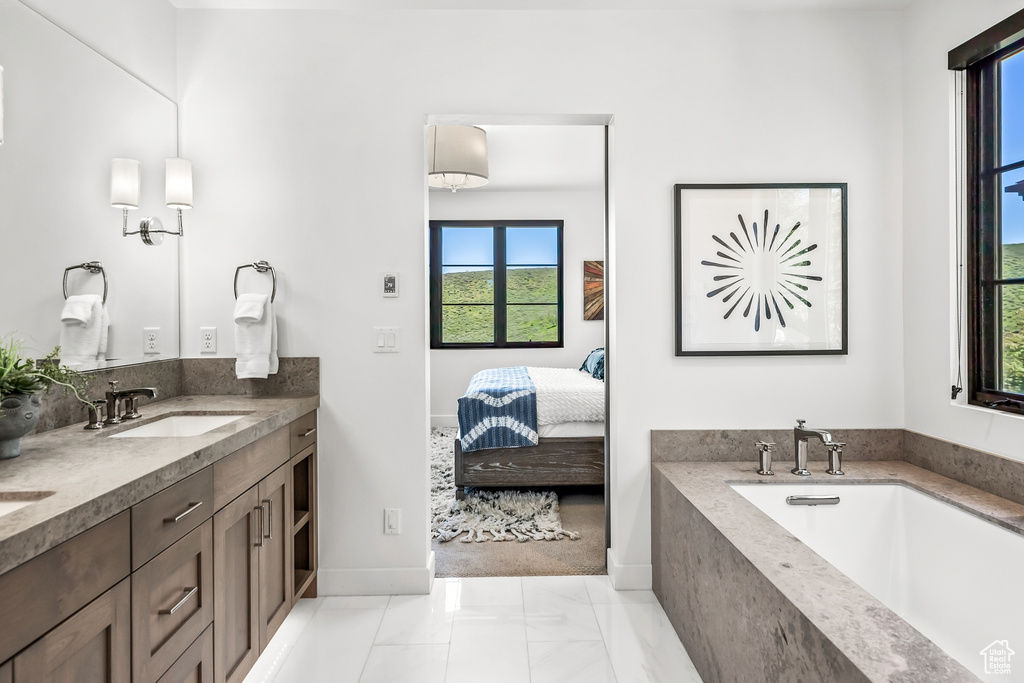 Bathroom with connected bathroom, double vanity, a bath, a sink, and baseboards