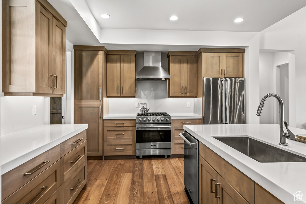 Kitchen with a sink, high end appliances, wall chimney range hood, light countertops, and dark wood finished floors