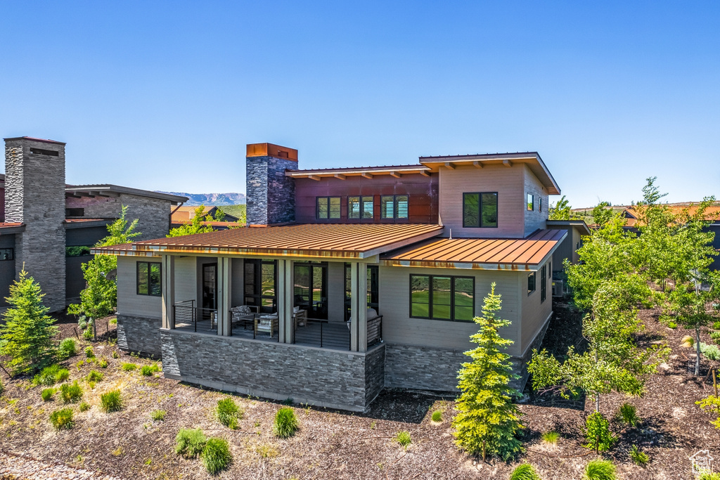 Back of property with metal roof, a standing seam roof, stone siding, and a chimney