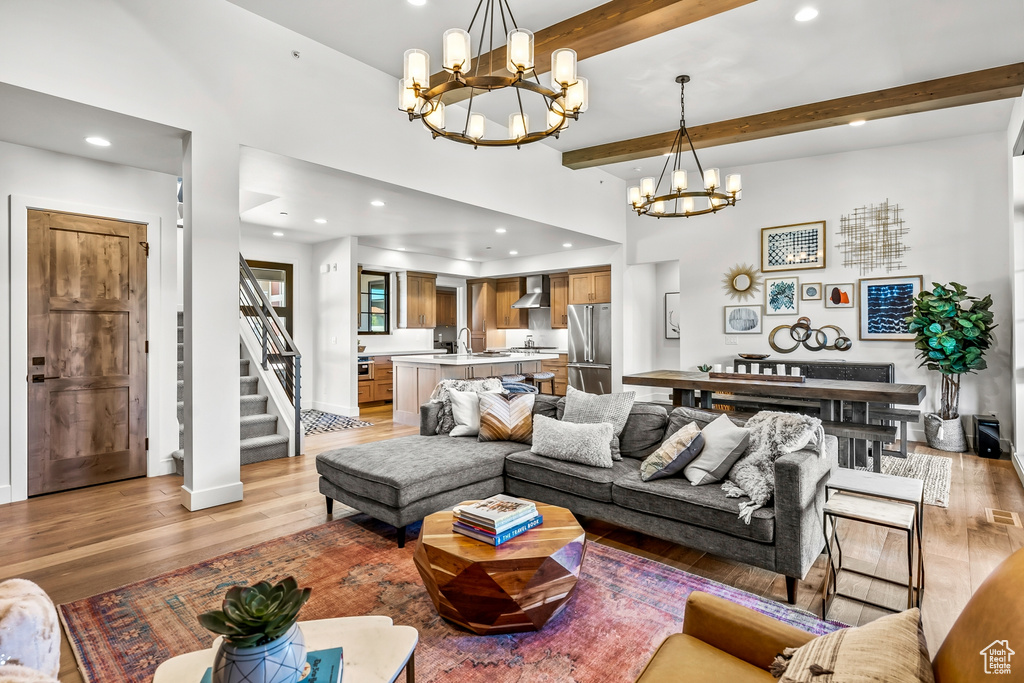 Living room with beamed ceiling, light wood-type flooring, recessed lighting, a notable chandelier, and stairs