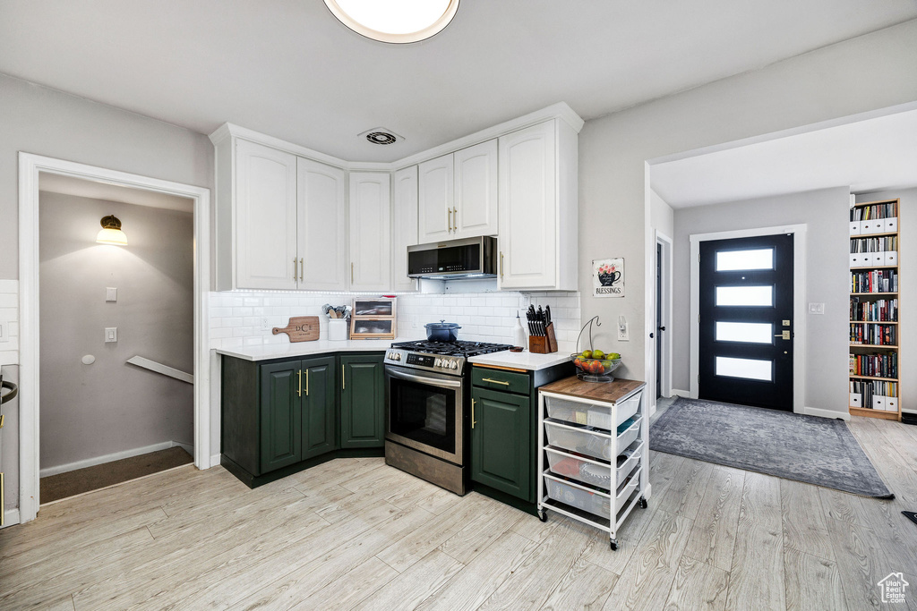Kitchen with white cabinetry, green cabinetry, stainless steel appliances, light hardwood / wood-style floors, and backsplash