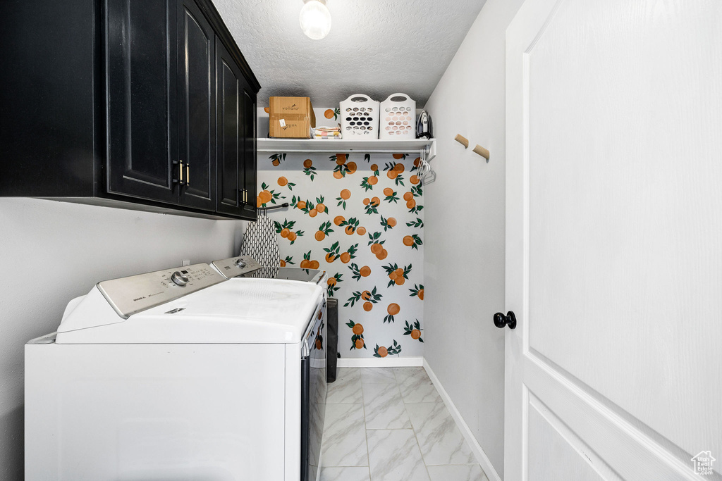 Clothes washing area with cabinets, washer and clothes dryer, and a textured ceiling