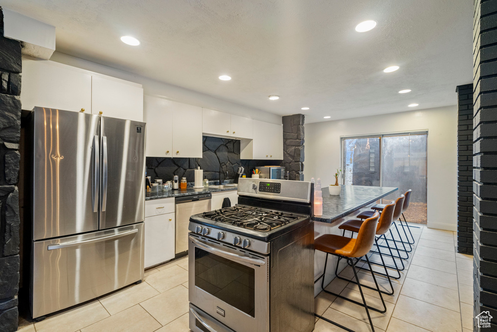 Kitchen with tasteful backsplash, a center island, a kitchen breakfast bar, stainless steel appliances, and white cabinets