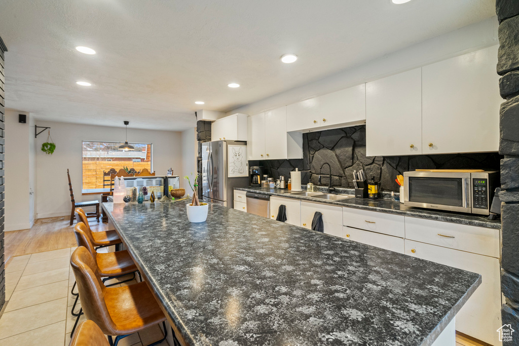 Kitchen with sink, a kitchen island, pendant lighting, stainless steel appliances, and white cabinets