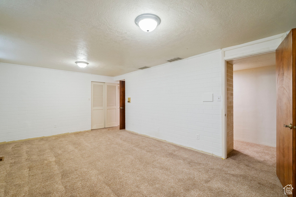 Basement featuring brick wall, light carpet, and a textured ceiling