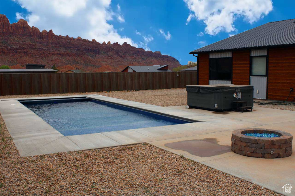 View of pool featuring a hot tub, a mountain view, a fire pit, and a patio