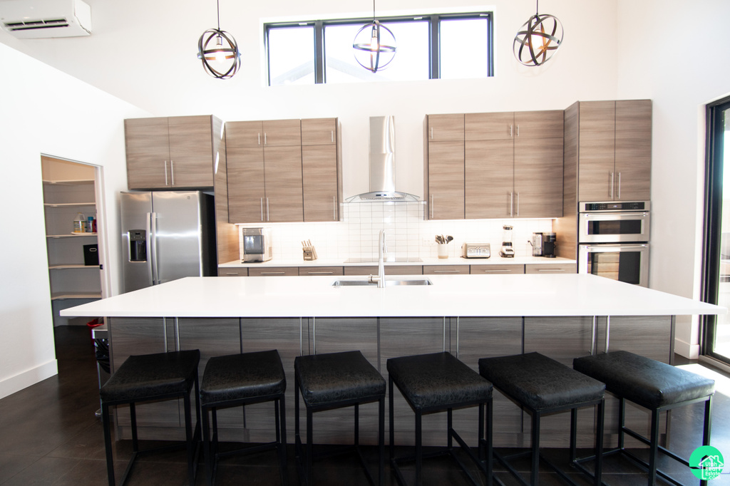 Kitchen with pendant lighting, a wall mounted AC, a kitchen bar, stainless steel appliances, and wall chimney exhaust hood