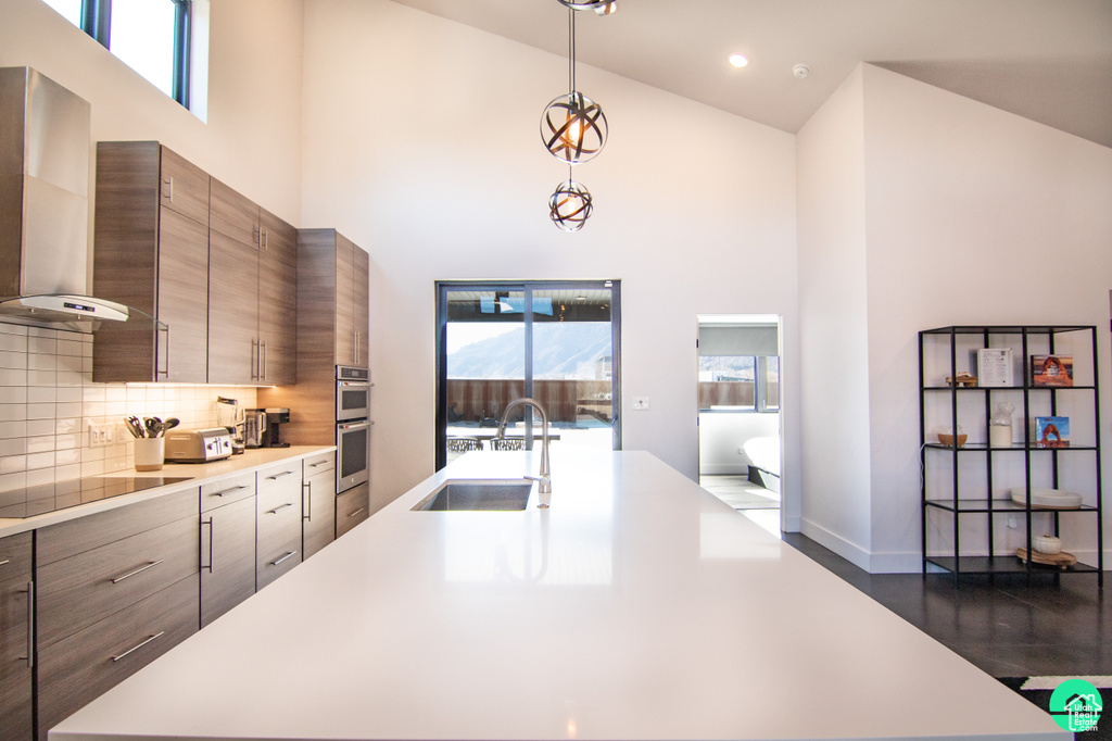 Kitchen with pendant lighting, sink, a towering ceiling, black electric stovetop, and wall chimney exhaust hood