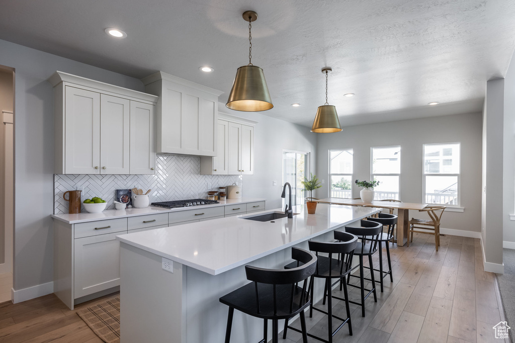 Kitchen featuring baseboards, a sink, gas stovetop, light countertops, and tasteful backsplash