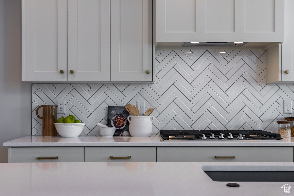 Kitchen featuring backsplash, light countertops, stainless steel gas stovetop, and white cabinets