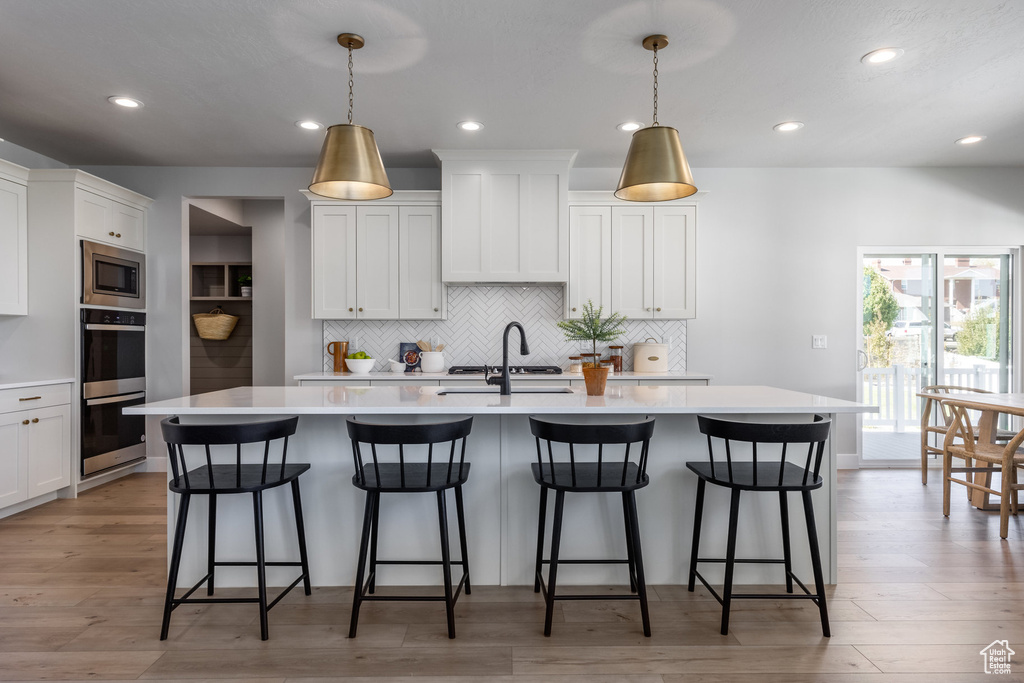 Kitchen featuring appliances with stainless steel finishes, light countertops, a center island with sink, backsplash, and a kitchen breakfast bar
