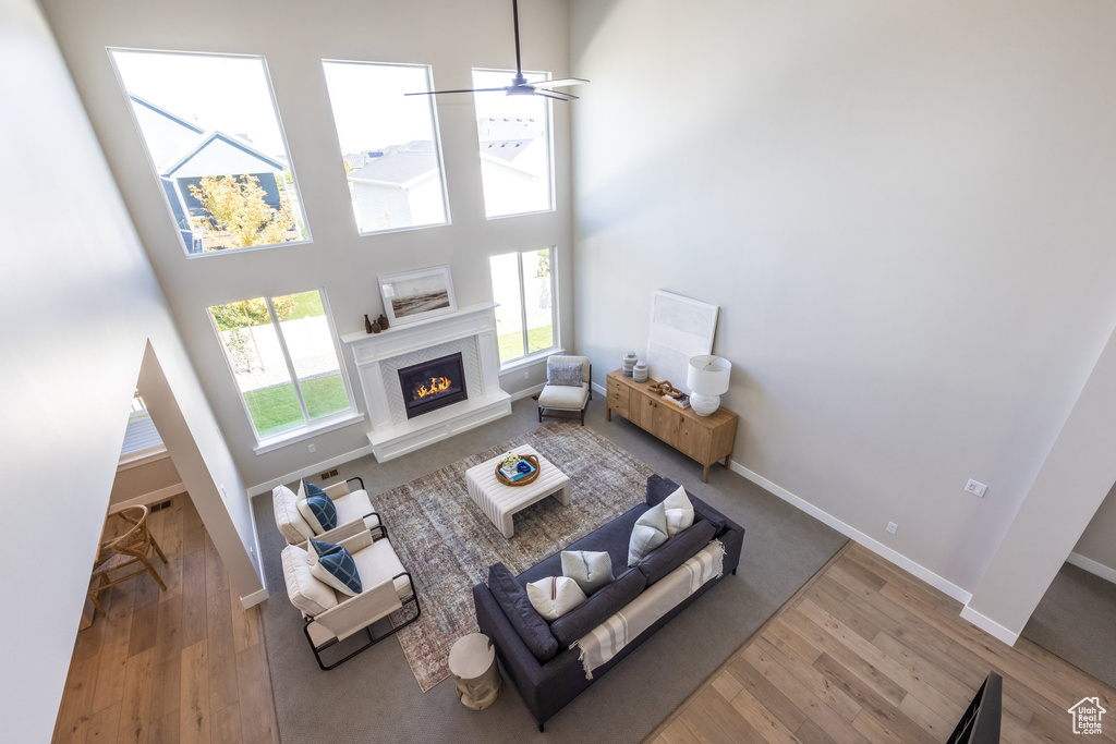 Living room featuring a premium fireplace, wood finished floors, baseboards, a ceiling fan, and a towering ceiling
