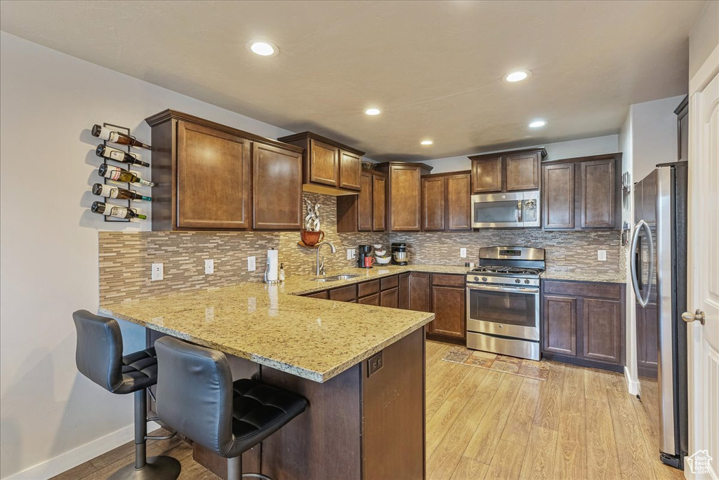 Kitchen with sink, light hardwood / wood-style flooring, stainless steel appliances, light stone counters, and kitchen peninsula